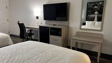 A hotel room with a bed, a desk with a television, a chair, a microwave, and a small table.