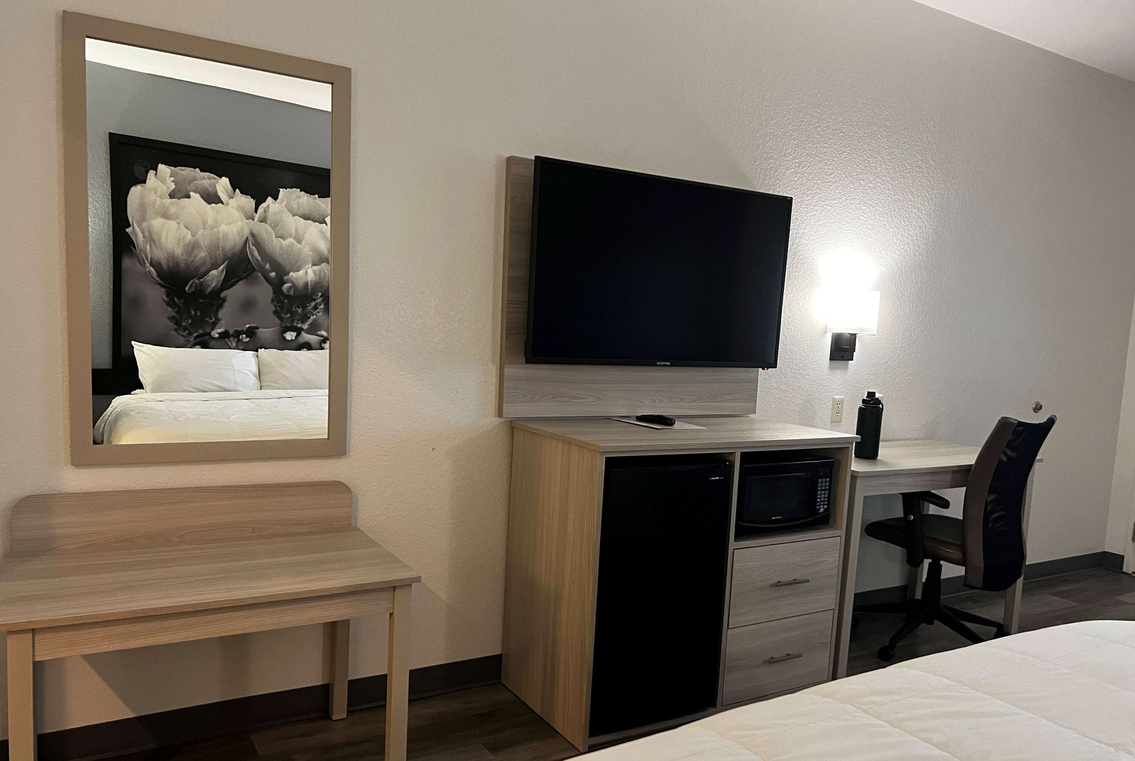 Habitación de hotel con cama, escritorio con televisor de pantalla plana, microondas, refrigerador, silla y mesita de noche.