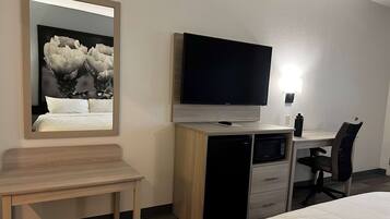 Habitación de hotel con cama, escritorio con televisor de pantalla plana, microondas, refrigerador, silla y mesita de noche.