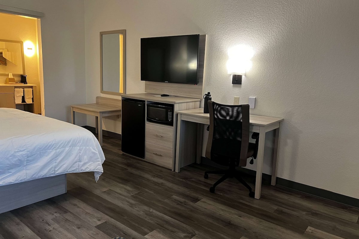 Quarto de hotel com cama, escrivaninha com computador, televisão e uma cadeira.