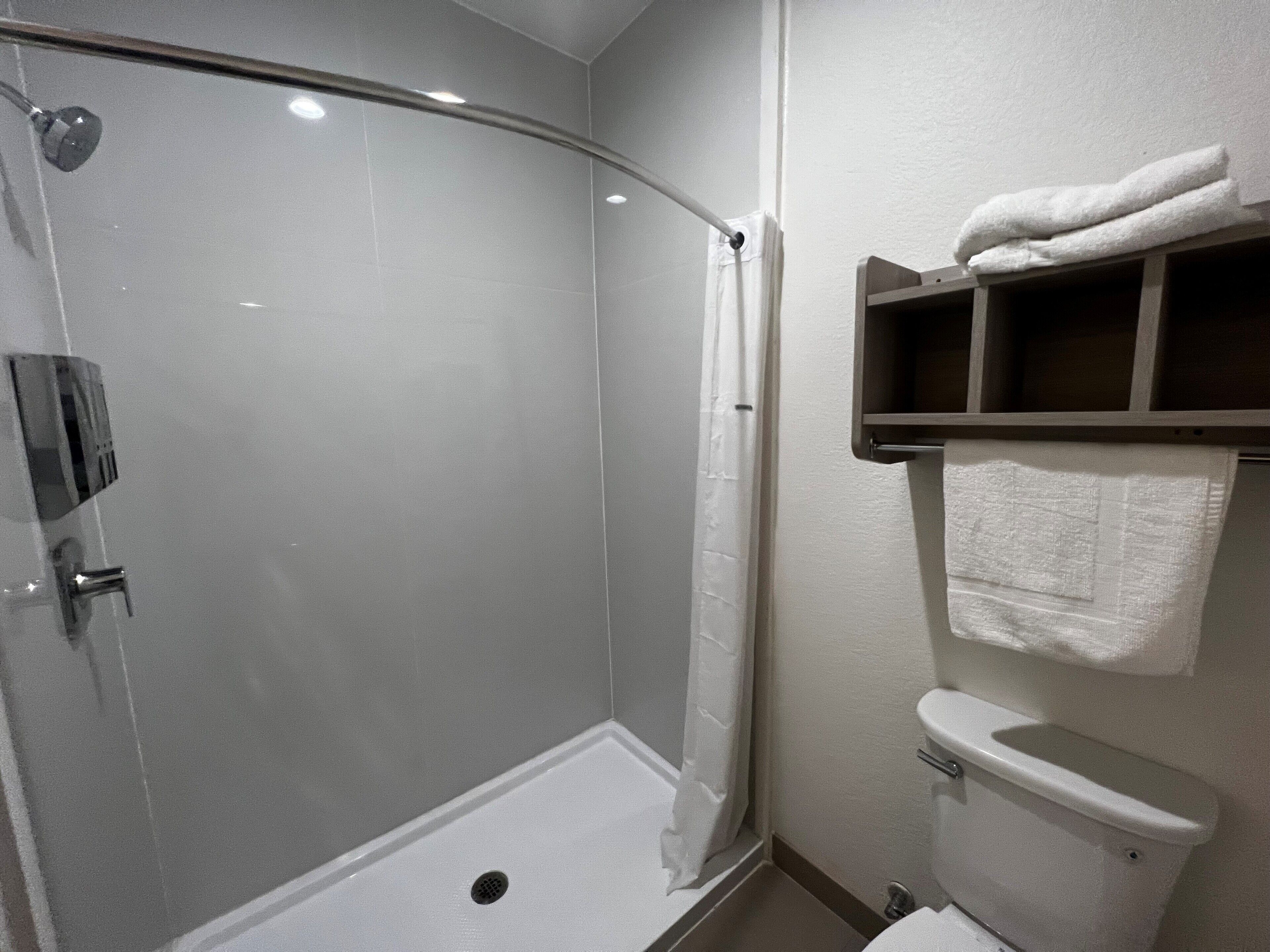 A bathroom with a glass-enclosed shower, a toilet, and a towel rack with folded towels.