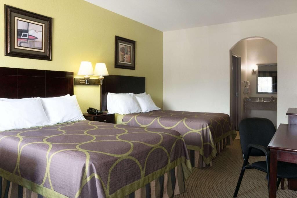 Une chambre d’hôtel avec deux lits, un bureau, une chaise, un téléphone et deux lampes fixées au mur.