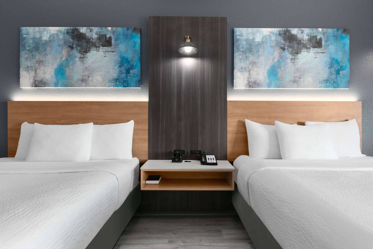Quarto de hotel com duas camas, mesa de cabeceira, telefone e arte abstrata nas paredes.