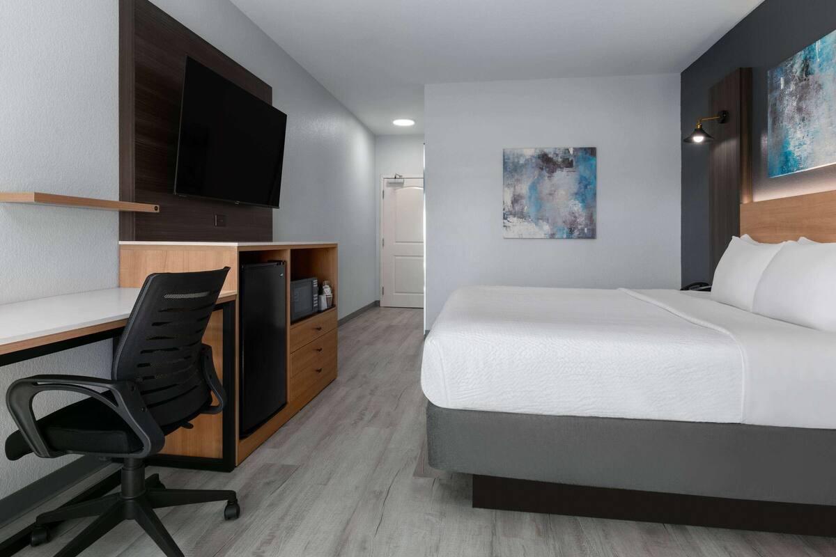 Quarto de hotel com cama, escrivaninha, cadeira, televisão e obras de arte nas paredes.