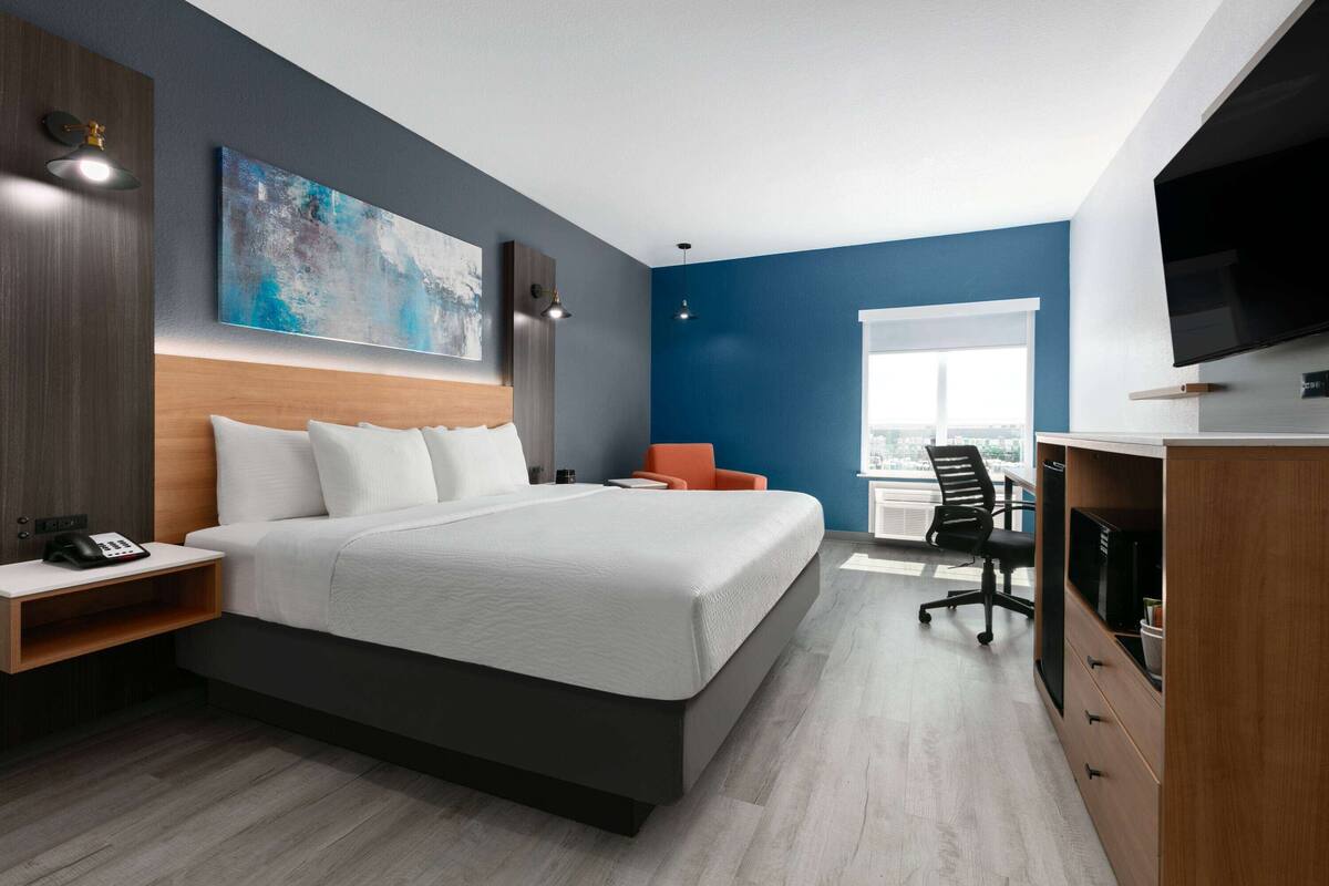 Quarto de hotel moderno com uma cama grande, uma escrivaninha, uma cadeira e uma televisão.