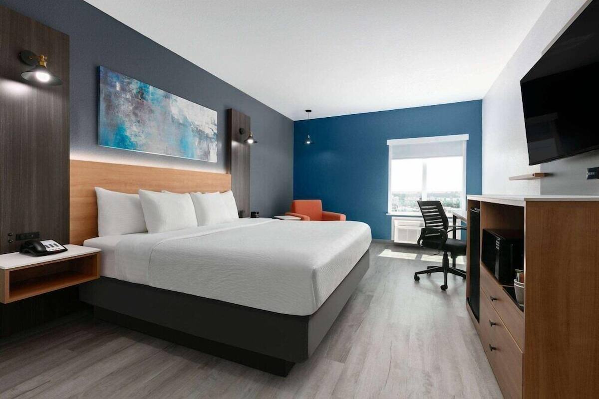 Quarto de hotel moderno com uma cama grande, escrivaninha, cadeira e televisão.
