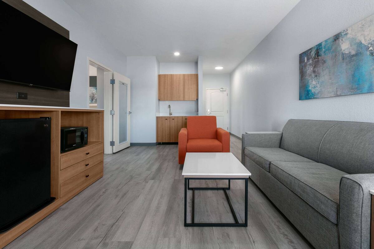 Uma sala de estar moderna com televisão de tela plana, armários de madeira, um sofá cinza e uma mesa de centro branca.