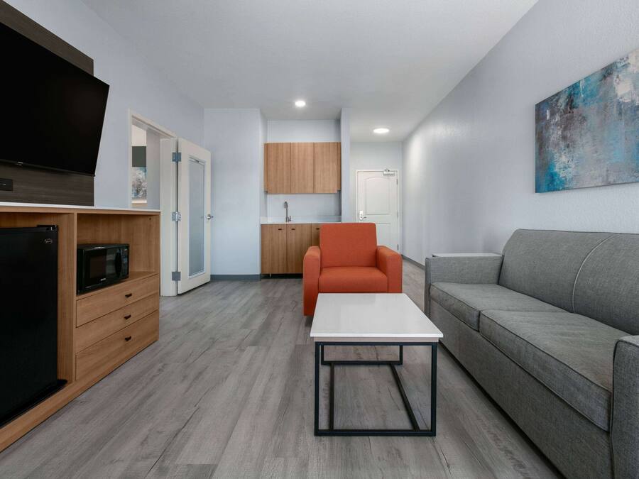 Una sala moderna con un televisor de pantalla plana, armarios de madera, un sofá gris y una mesa de centro blanca.