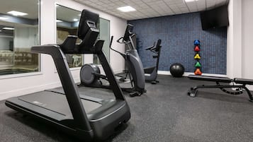 A gym with treadmills, elliptical machines, a bench, and a wall with exercise balls.