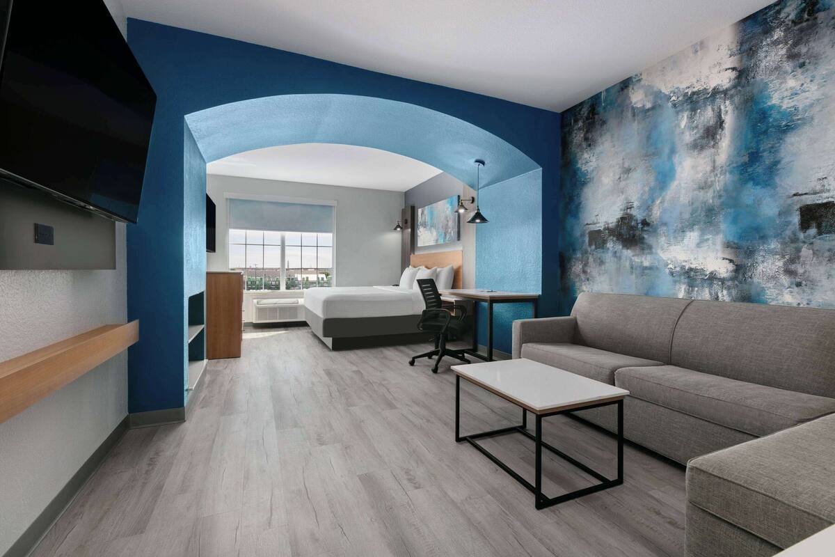 Quarto de hotel moderno com uma cama grande, um sofá, uma escrivaninha e uma televisão.