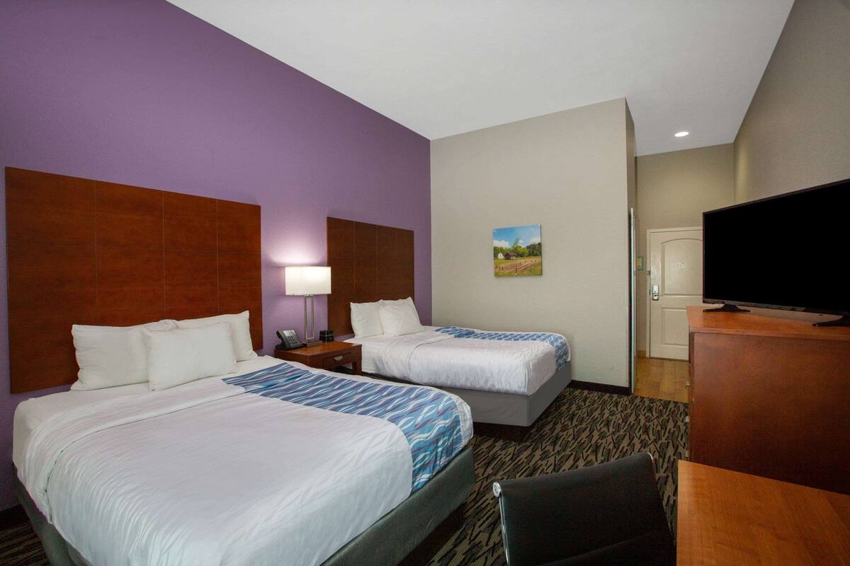 A hotel room with two beds, a television, a desk, and a painting on the wall.