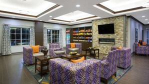 A spacious lobby with patterned seating, a stone accent wall, a flat-screen TV, and a snack bar. - La Quinta Inn & Suites by Wyndham Tupelo (Tupelo)