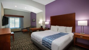 A hotel room with a large bed, a desk, a chair, a TV, and a window with patterned curtains. - La Quinta Inn & Suites by Wyndham Tupelo (Tupelo)