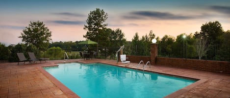 A rectangular swimming pool with a tiled deck, surrounded by a brick wall and metal fencing.