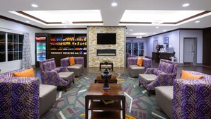 A lobby with patterned sofas, a coffee machine, a television, and a snack vending machine. - La Quinta Inn & Suites by Wyndham Tupelo (Tupelo)