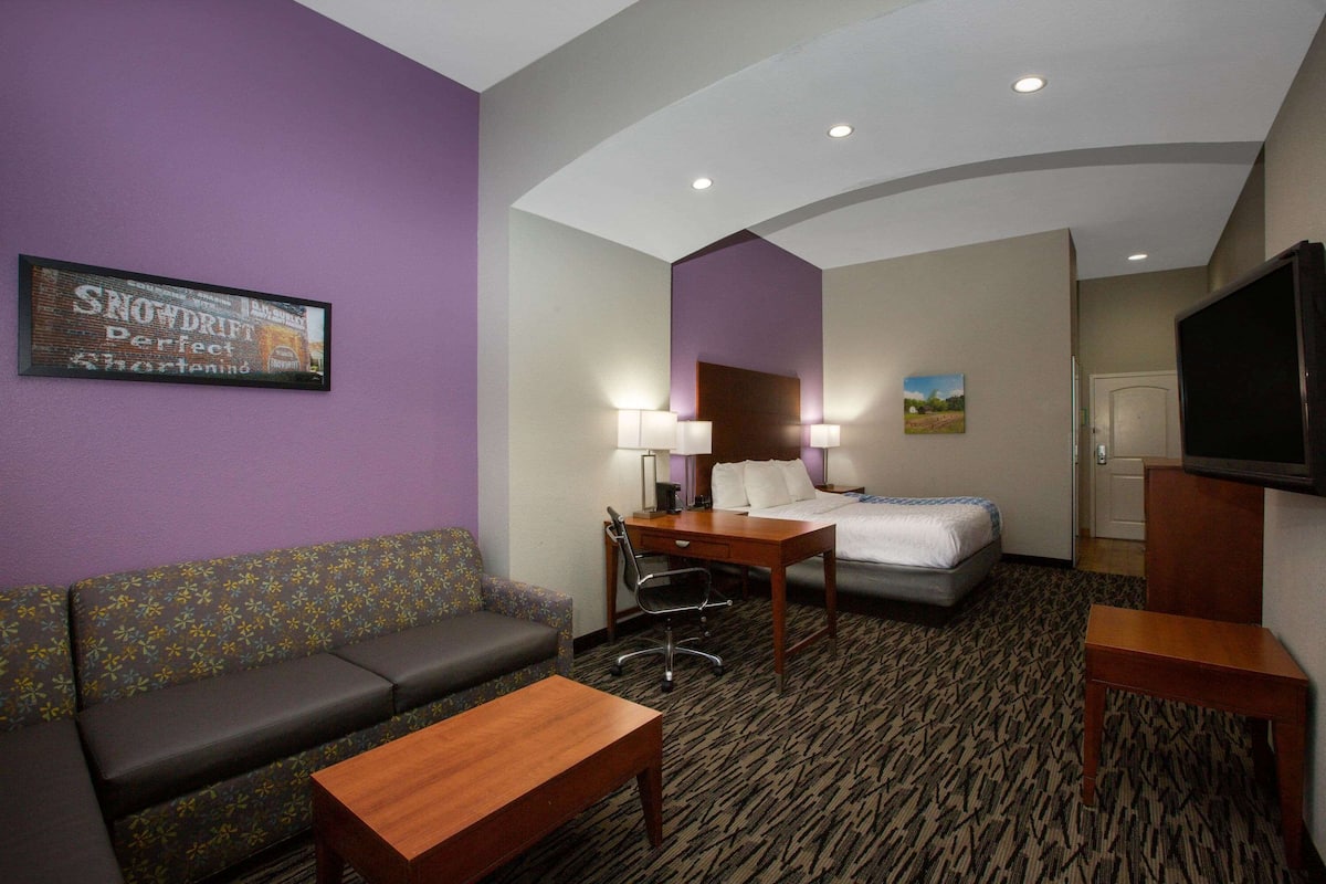 A hotel room with a sofa, a desk, a bed, and a TV.
