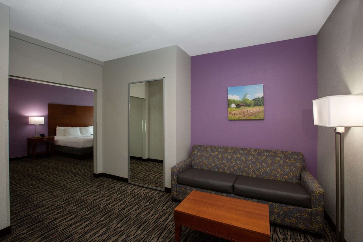 A hotel room with a sofa, a small table, a painting on the wall, and a mirror reflecting the room.