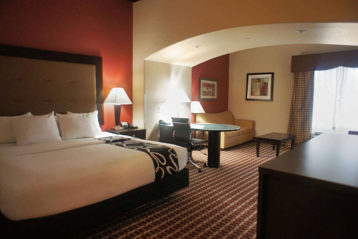 Una habitación de hotel con una cama grande, un escritorio, una silla, un sofá y dos lámparas.
