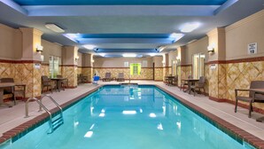 An indoor swimming pool with clear water, surrounded by lounge chairs and tables.