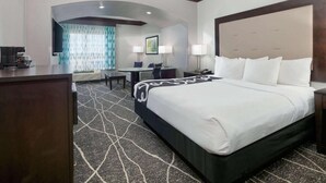 A hotel room with a large bed, a desk, a chair, and a view of the cityscape through the window.