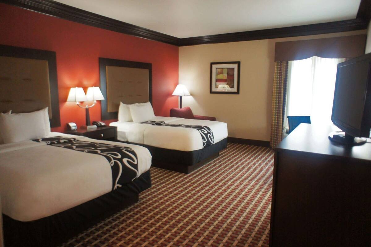Habitación de hotel con dos camas, un escritorio, televisor y ventana con cortinas.