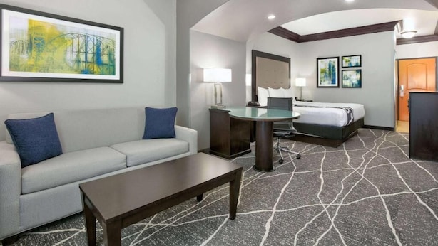 A hotel room with a sofa, a desk, a bed, and a large painting on the wall.