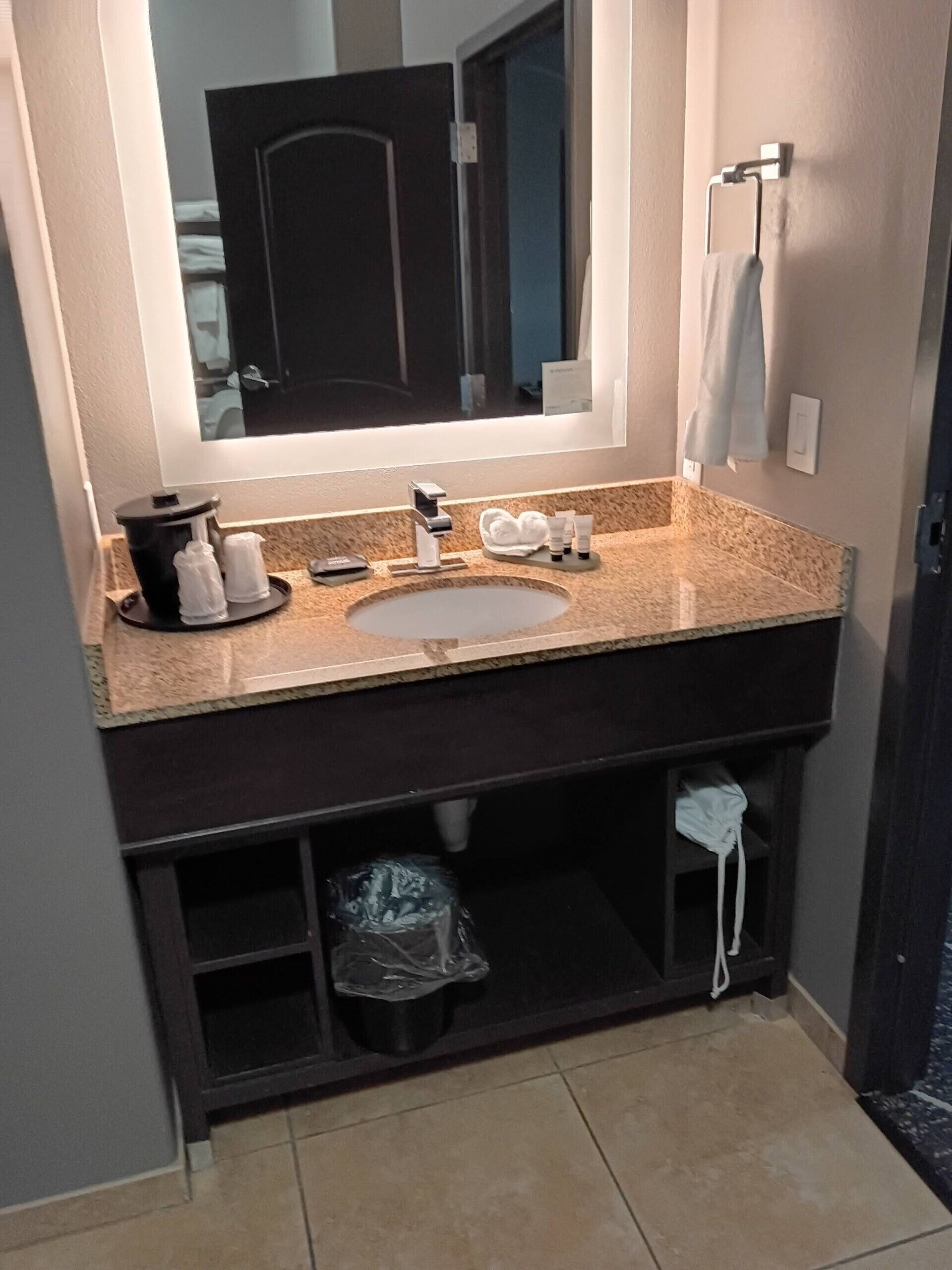 A bathroom with a sink, mirror, towel rack, and a trash bin.