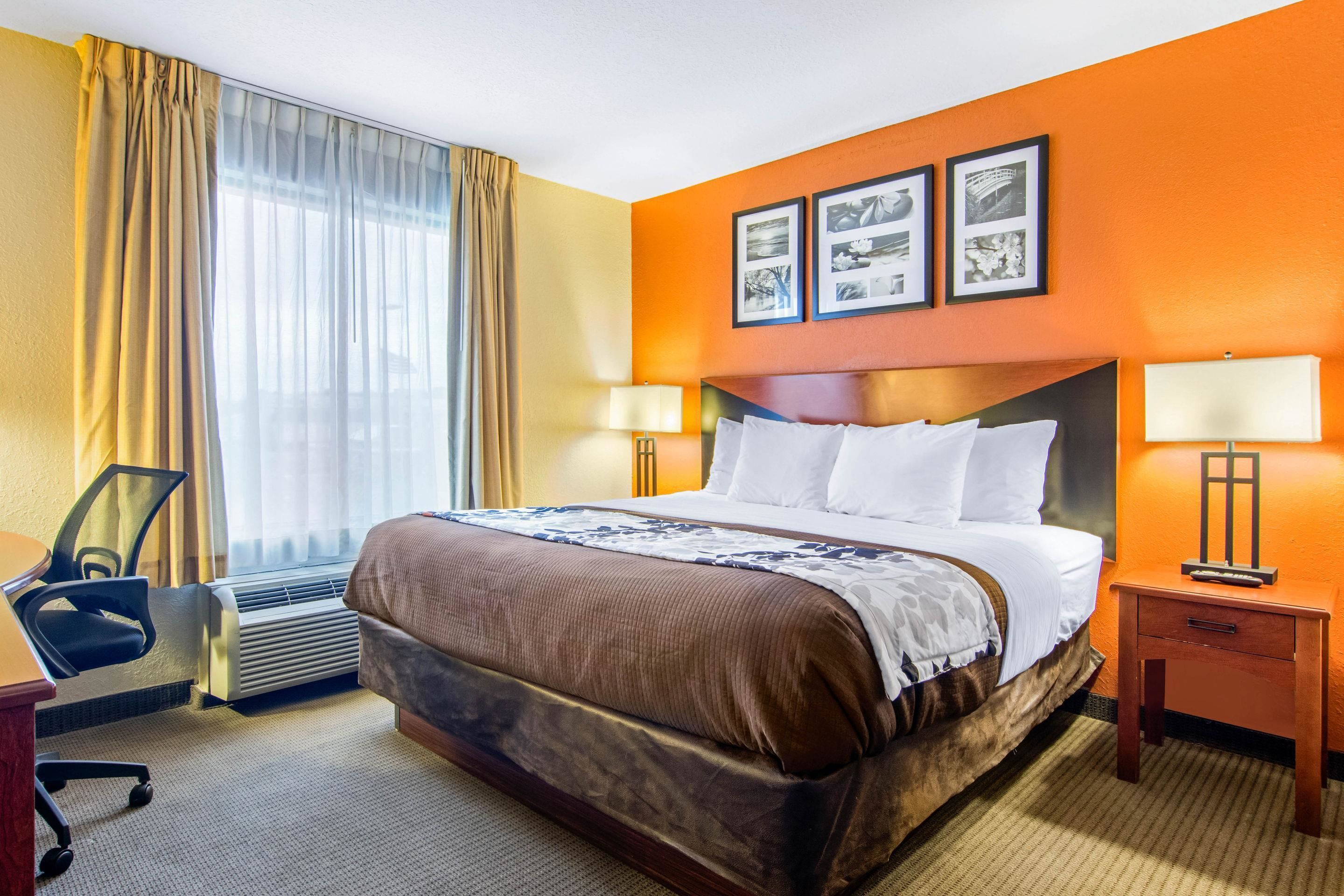 A hotel room with a large bed, a desk with a chair, two bedside lamps, and a window with curtains.