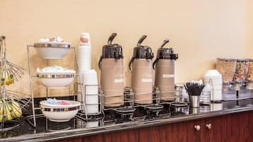 A breakfast bar with hot water dispensers, paper cups, and cereal containers.