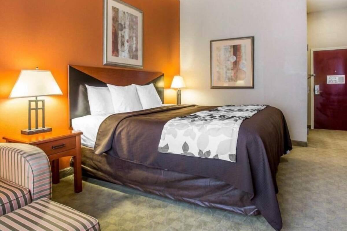 A hotel room with a bed, two bedside lamps, a chair, and two framed pictures on the wall.