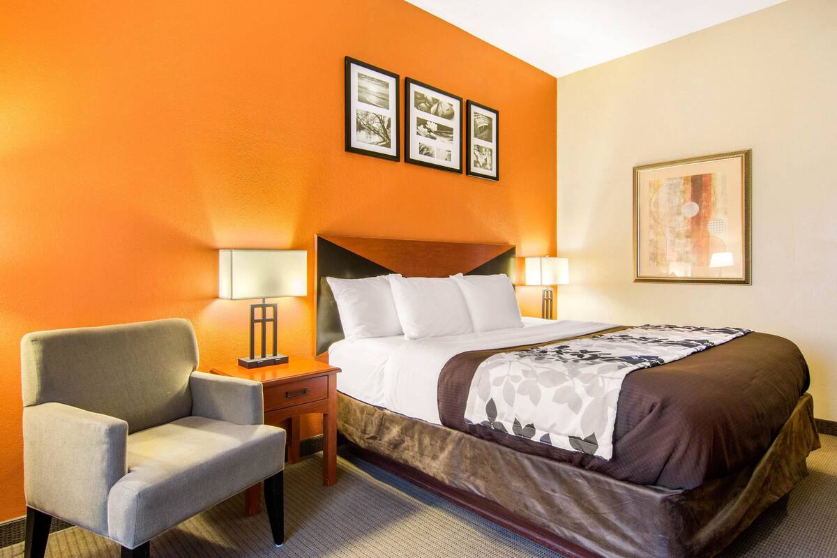A hotel room with a bed, two bedside lamps, a chair, and a wall with three framed pictures.
