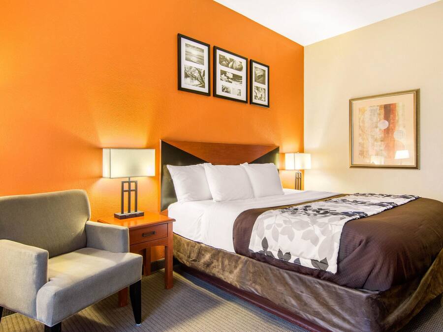 A hotel room with a bed, two bedside lamps, a chair, and a wall with three framed pictures.