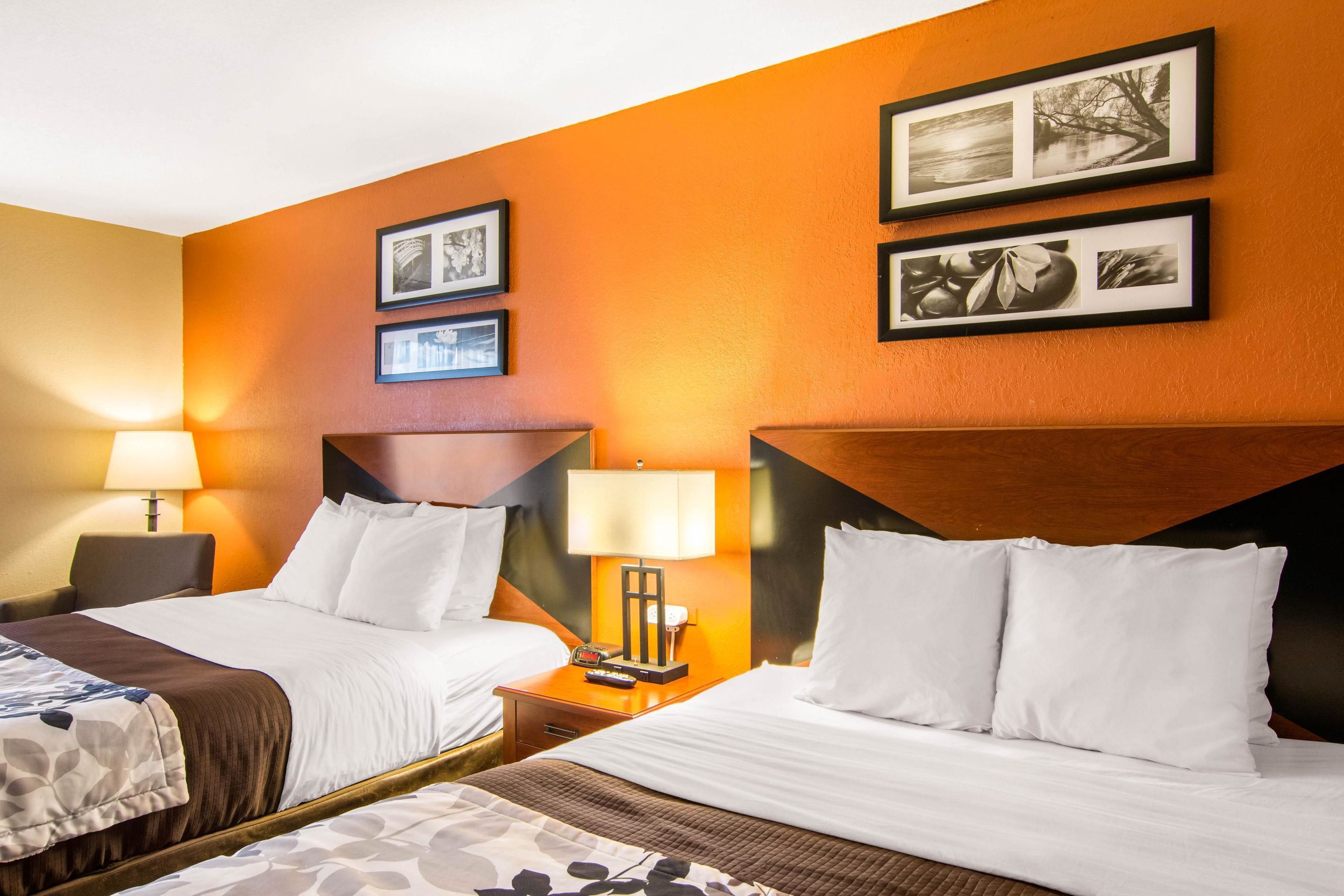 A hotel room with two beds, a nightstand with a lamp, and framed pictures on the wall.