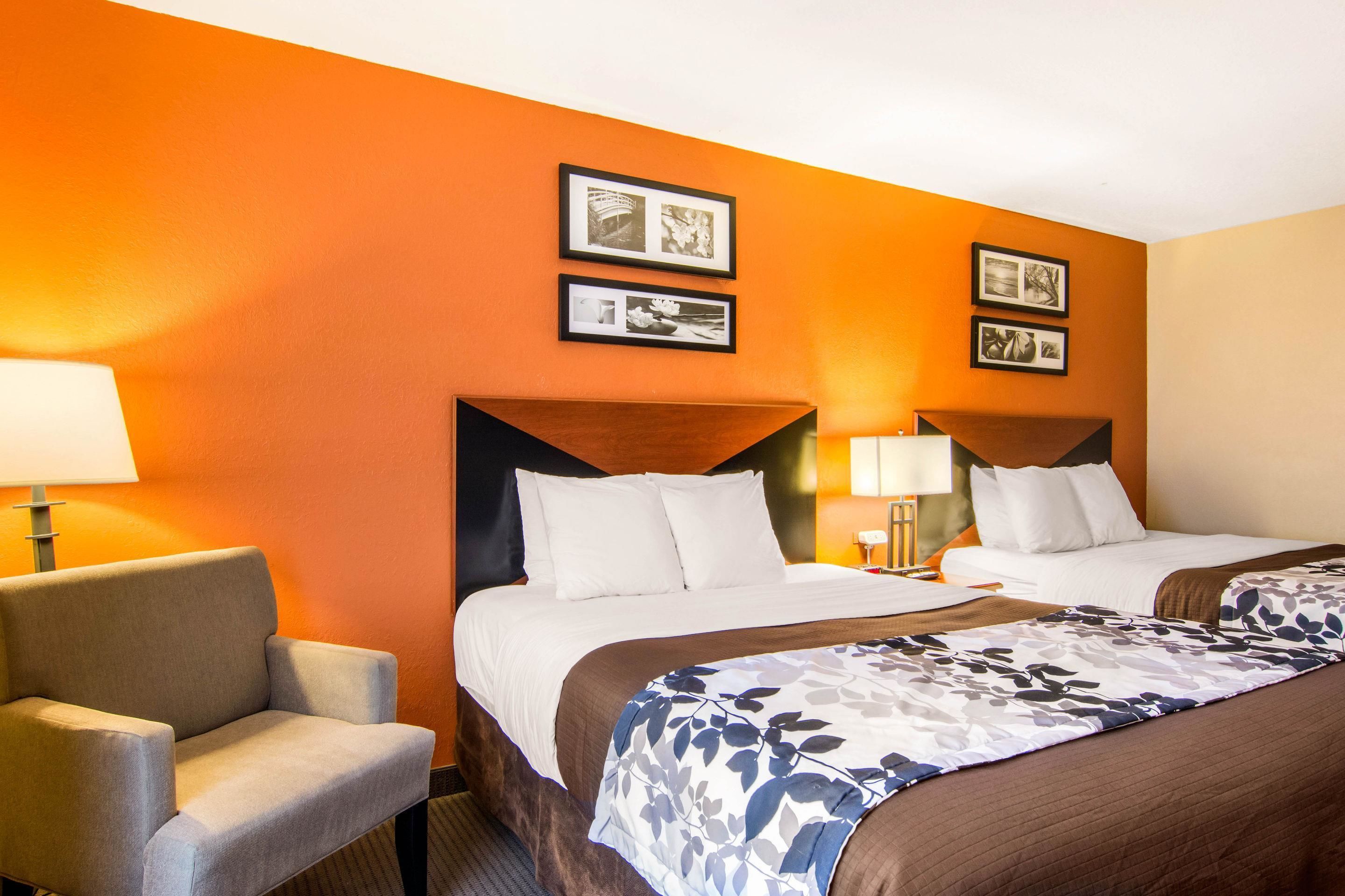 A hotel room with two beds, a chair, and framed pictures on the wall.