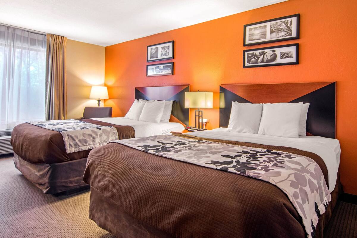 A hotel room with two beds, a large window with curtains, and a wall with framed pictures.