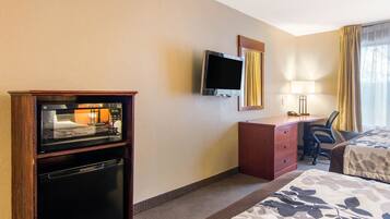 A hotel room with a bed, a desk with a chair, a television, and a minibar.