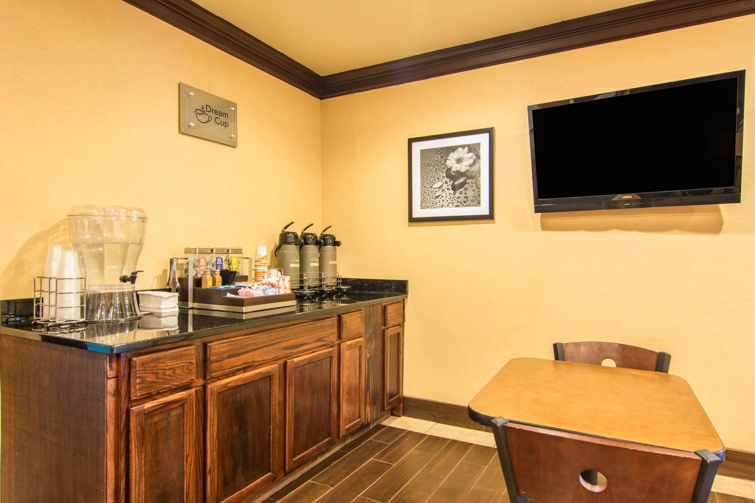 A kitchen with wooden cabinets, a coffee station, a framed picture, and a TV mounted on the wall.