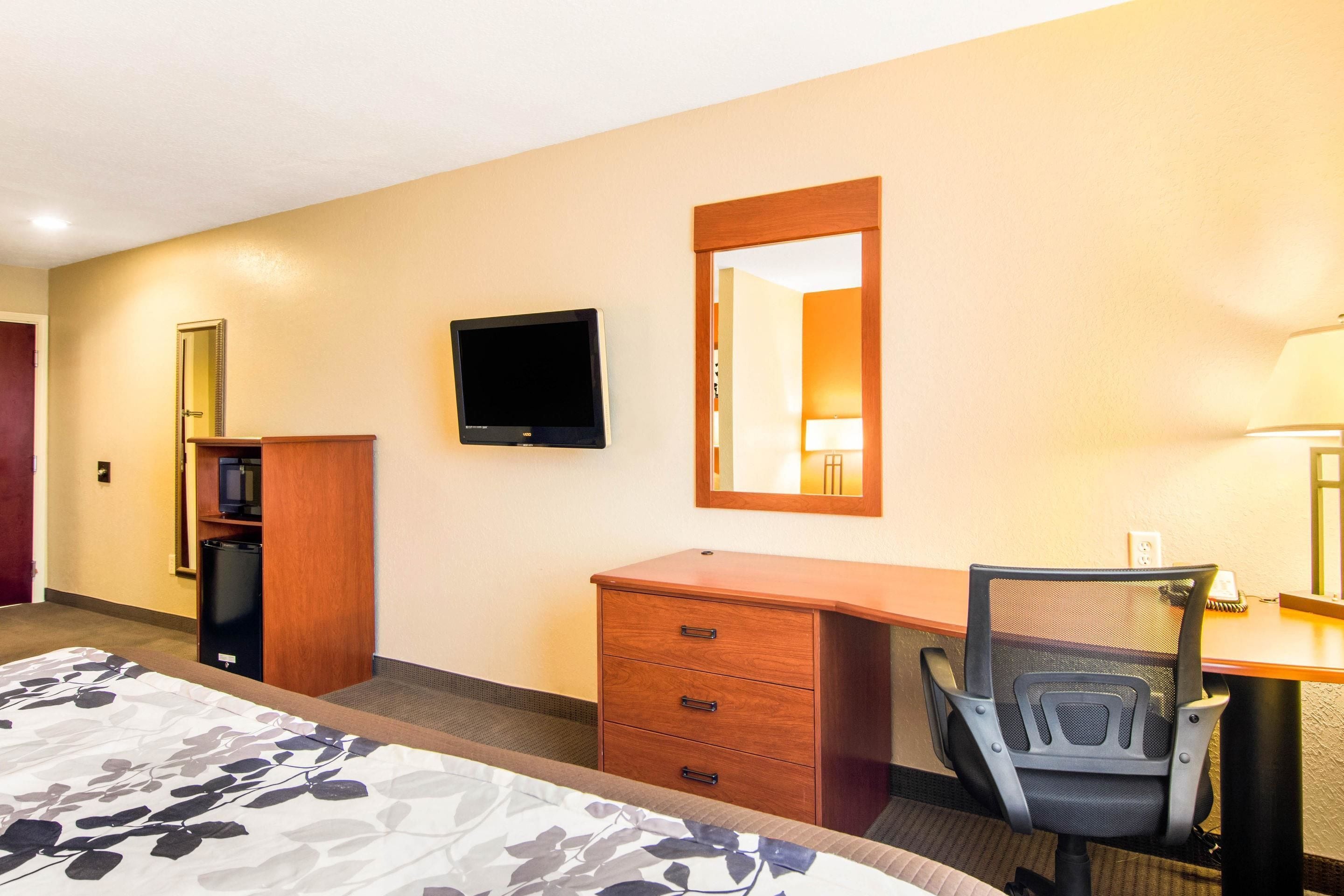 Une chambre d’hôtel équipée d’un lit, d’un bureau, d’une chaise, d’une télévision, d’un miroir et d’une armoire.