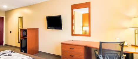 A hotel room with a bed, a desk, a chair, a television, a mirror, and a wardrobe.