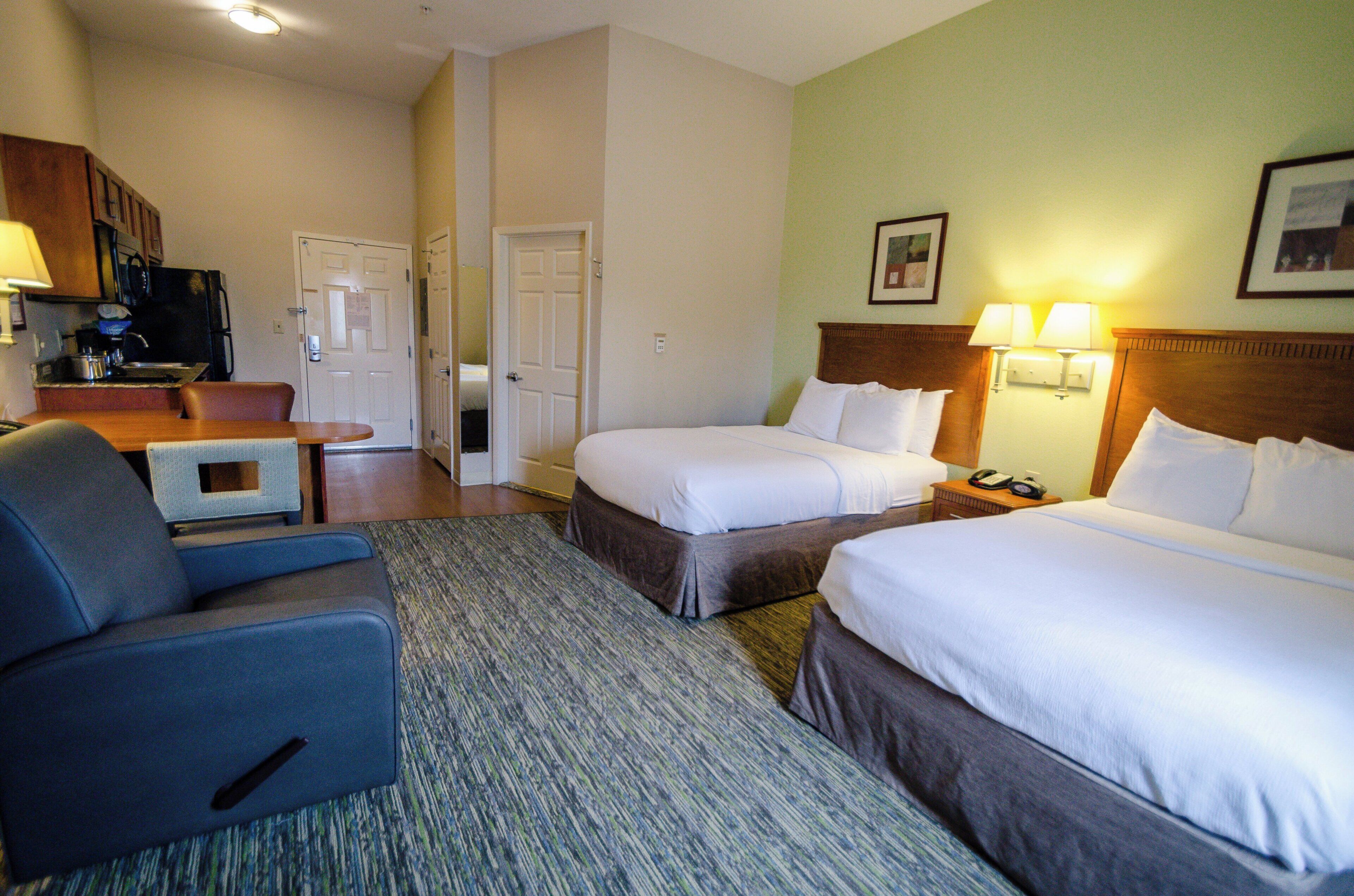A hotel room with two beds, a desk, a chair, and a kitchenette.