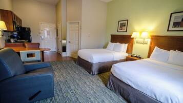A hotel room with two beds, a desk, a chair, and a kitchenette.