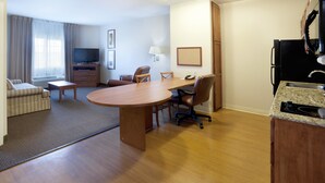 Une chambre d’hôtel équipée d’une table à manger, de chaises, d’un canapé, d’une télévision, d’une lampe, d’un réfrigérateur et d’un comptoir de cuisine.