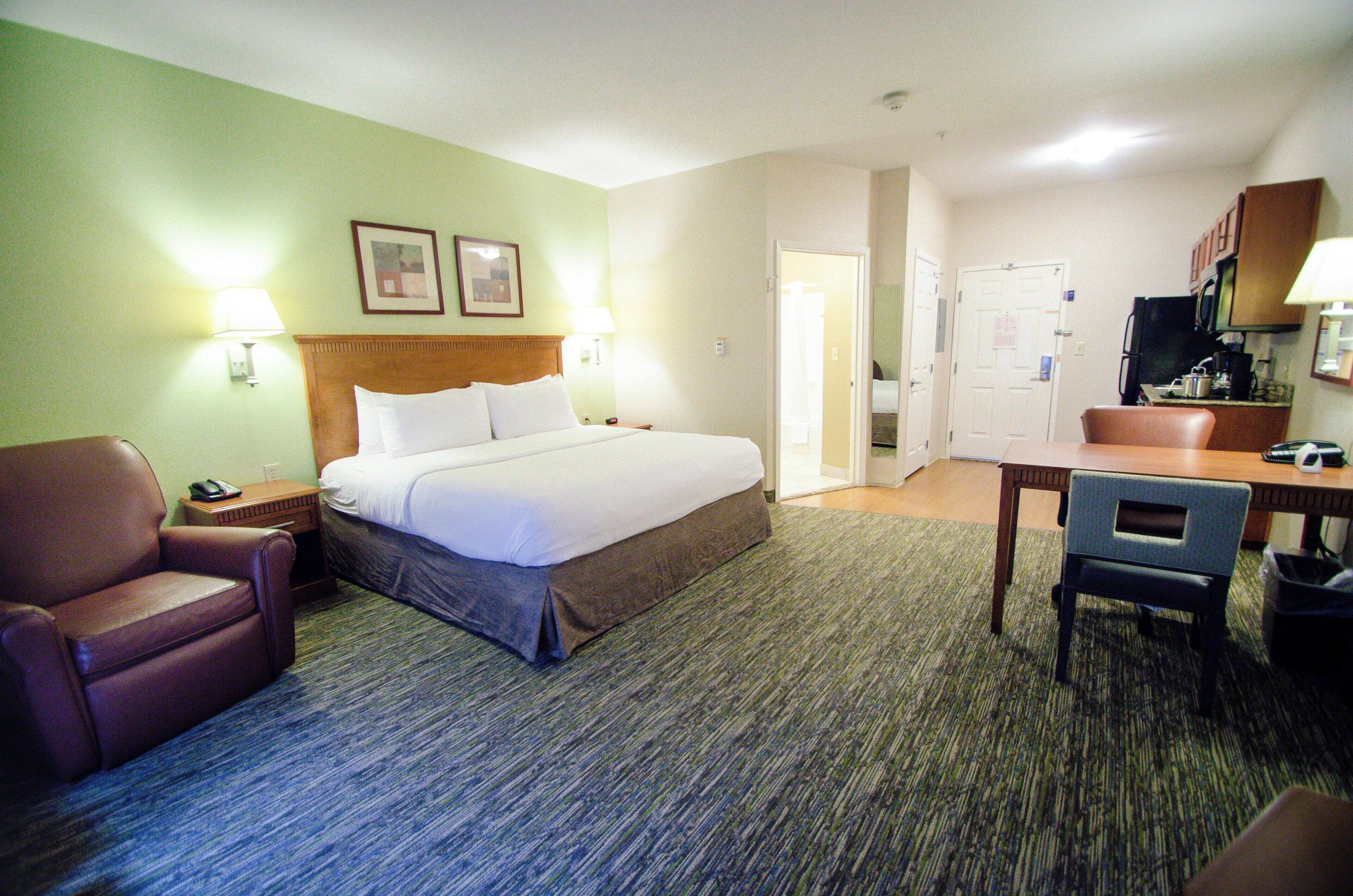 A hotel room with a bed, a desk, a chair, a TV, and a door leading to a bathroom.
