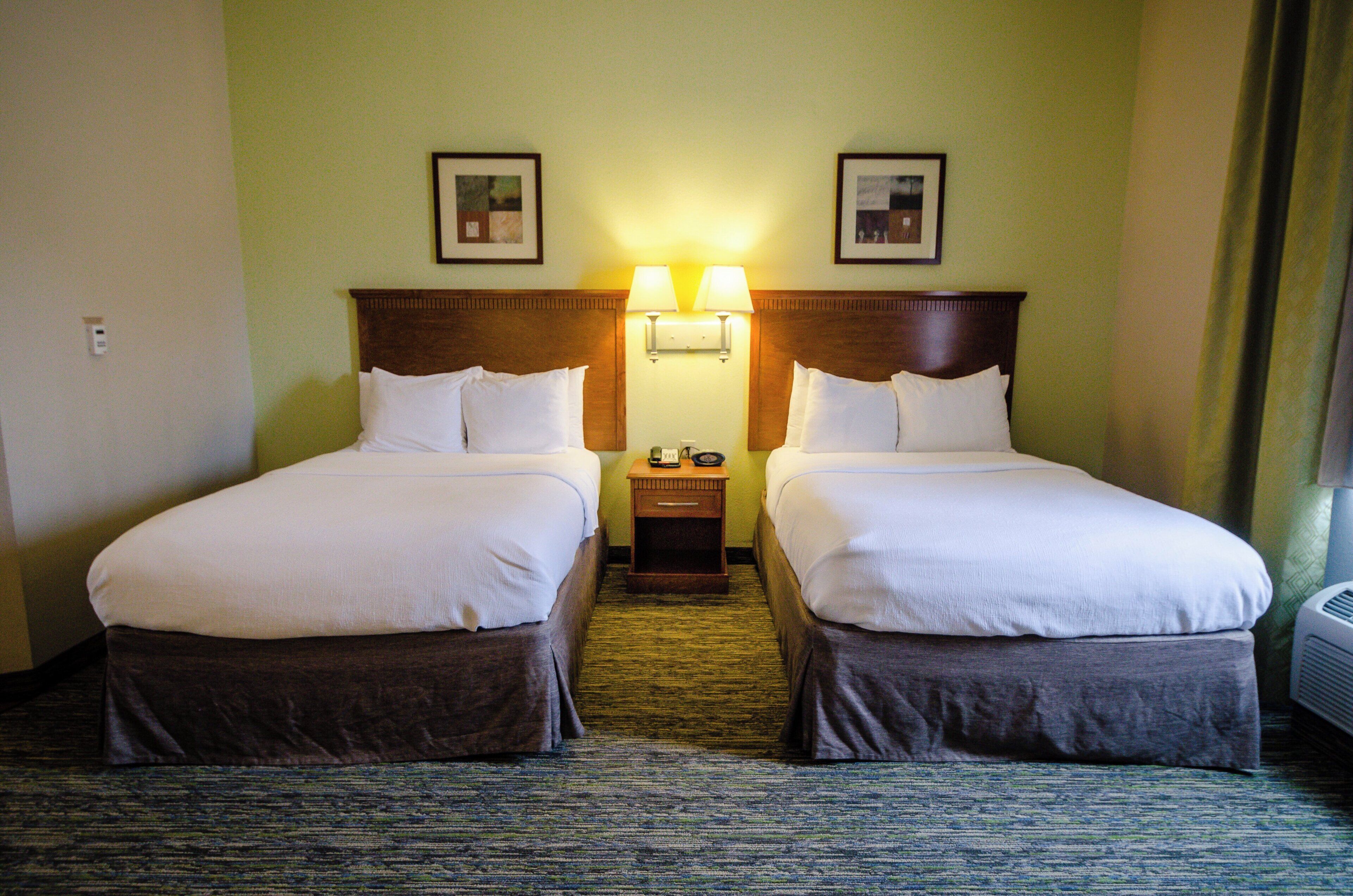 A hotel room with two beds, a nightstand, a lamp, and a picture on the wall.