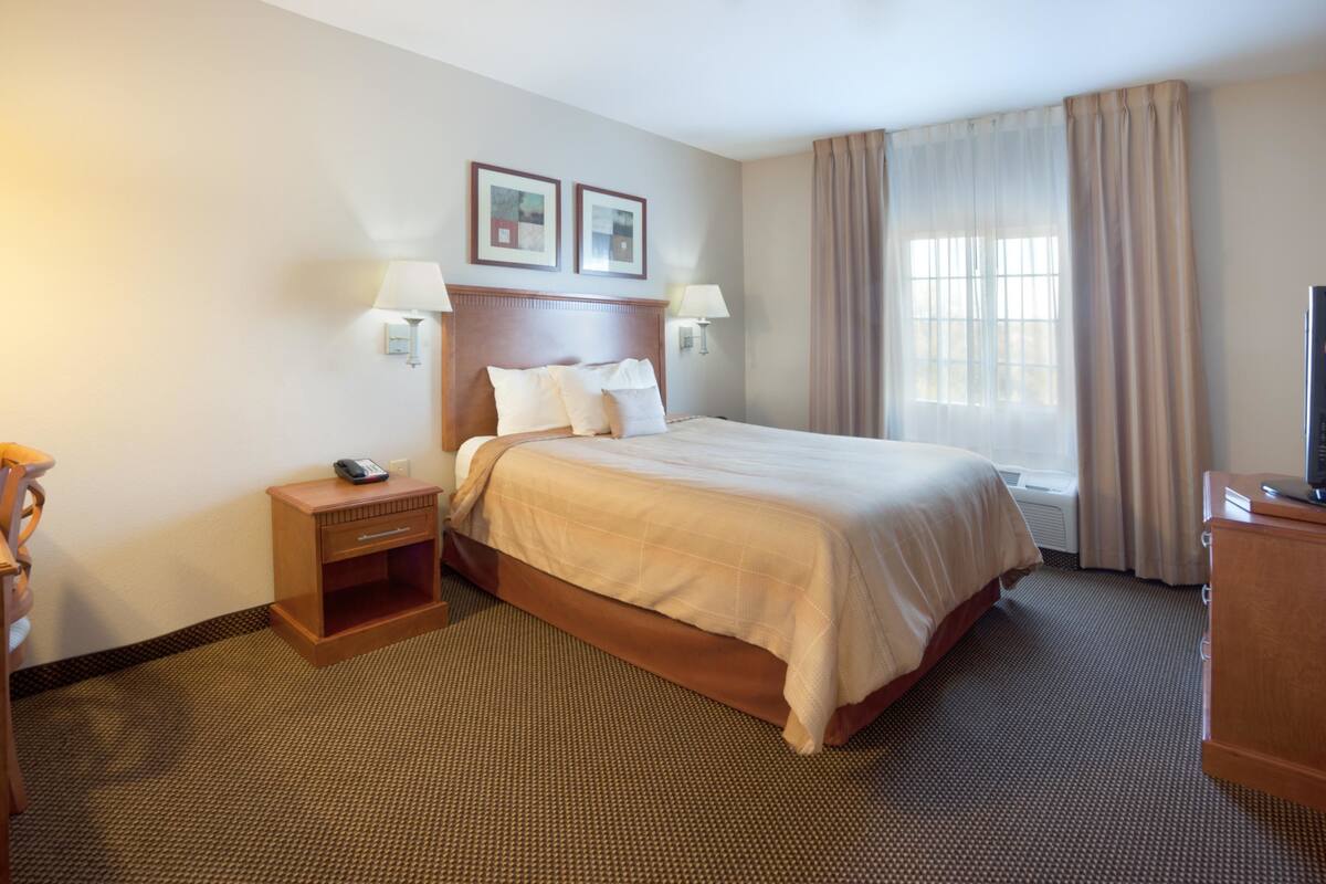 Een hotelkamer met een groot bed, nachtkastjes, een televisie en een raam met gordijnen.
