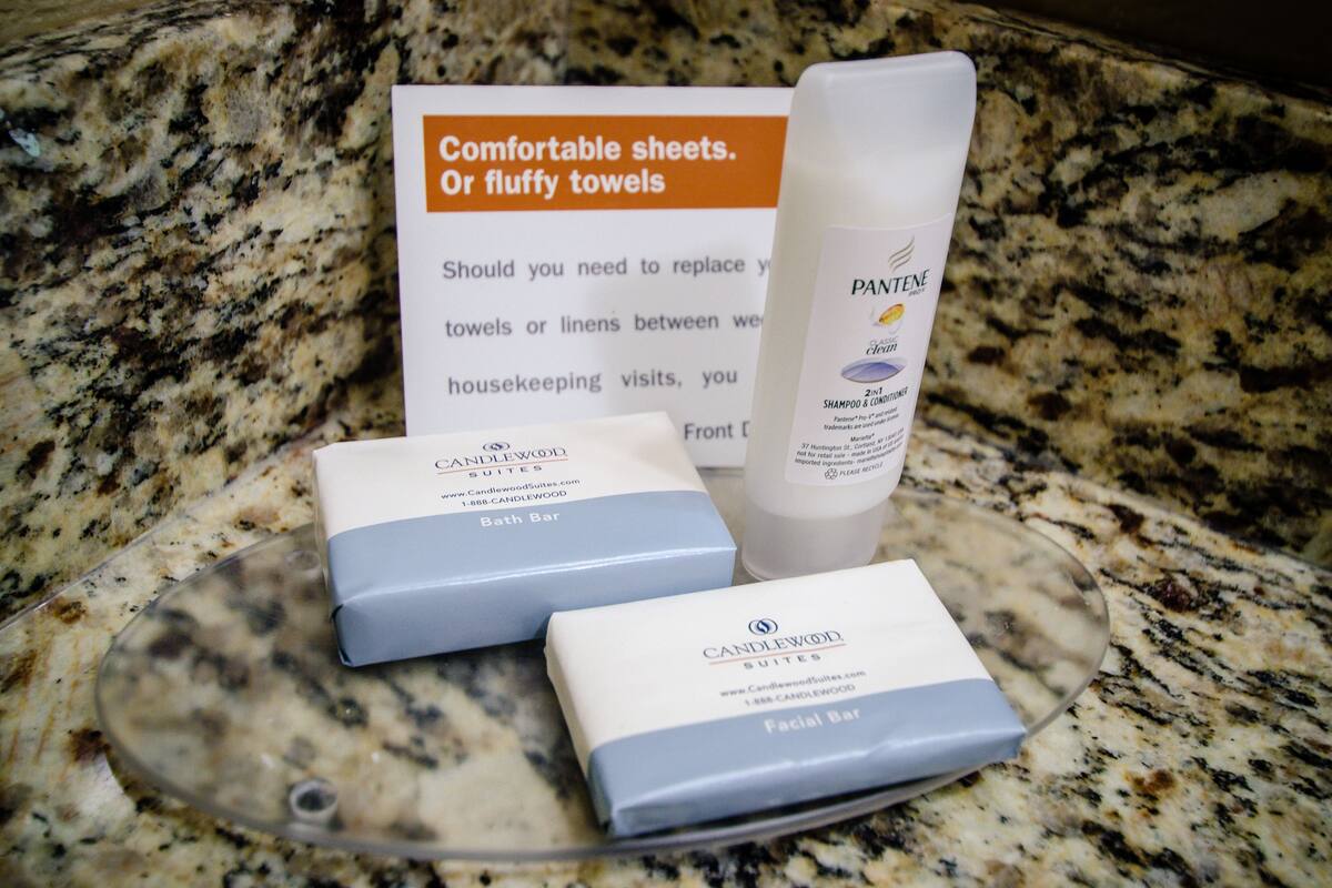 Een badkamermeubel met een bordje over het vervangen van handdoeken, een fles Pantene shampoo en twee zeepjes van Candlewood Suites.