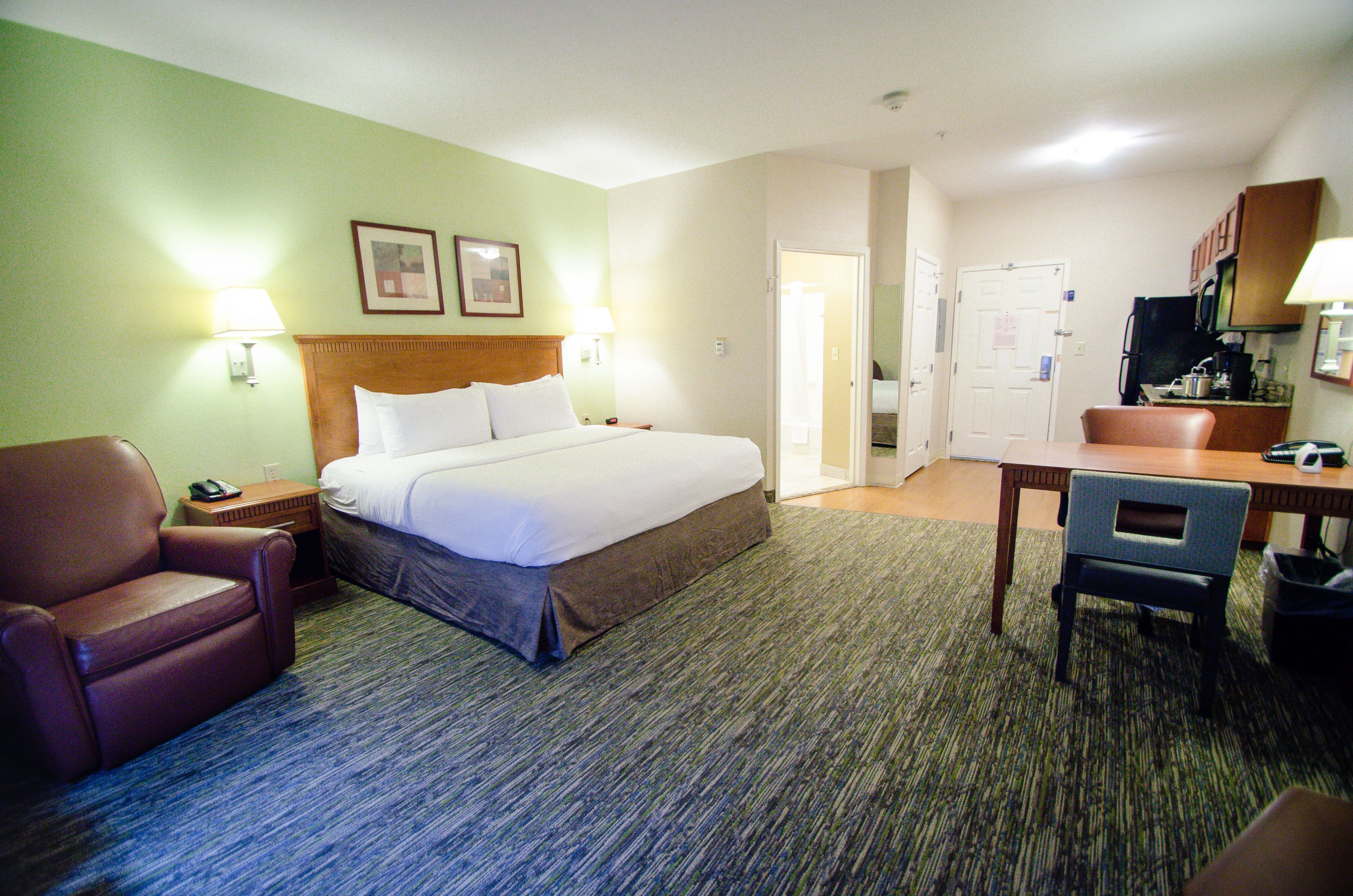 Quarto de hotel com cama, escrivaninha, cadeira, televisão e porta que dá para outro cômodo.