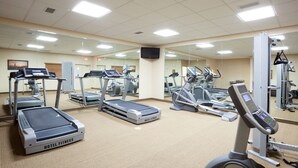 Une salle de sport d’hôtel équipée de tapis de course, de vélos elliptiques et d’un vélo d’appartement.