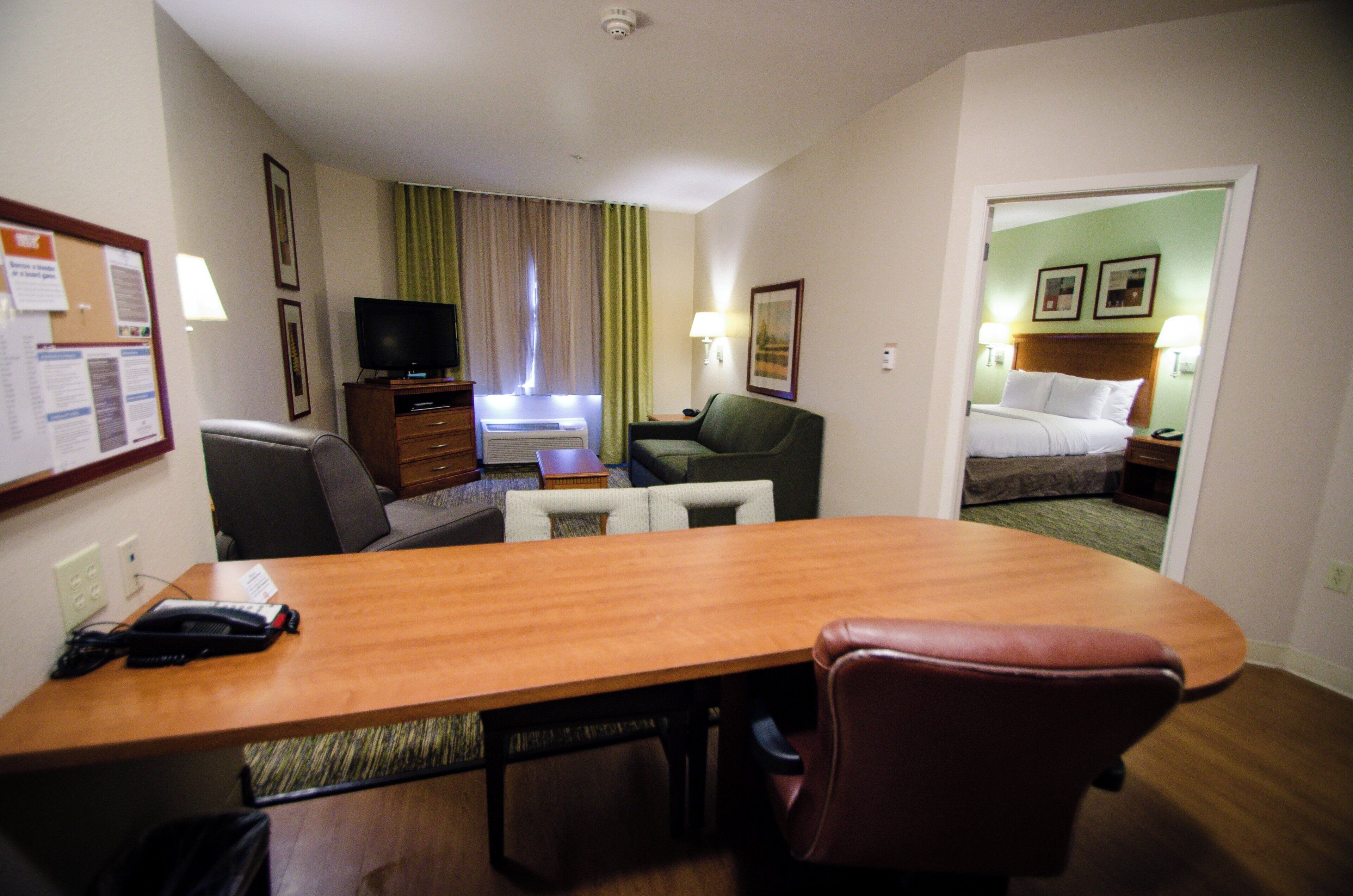 Una habitación de hotel con un escritorio de madera, televisor, sofá, cama y mesita de noche con lámpara.