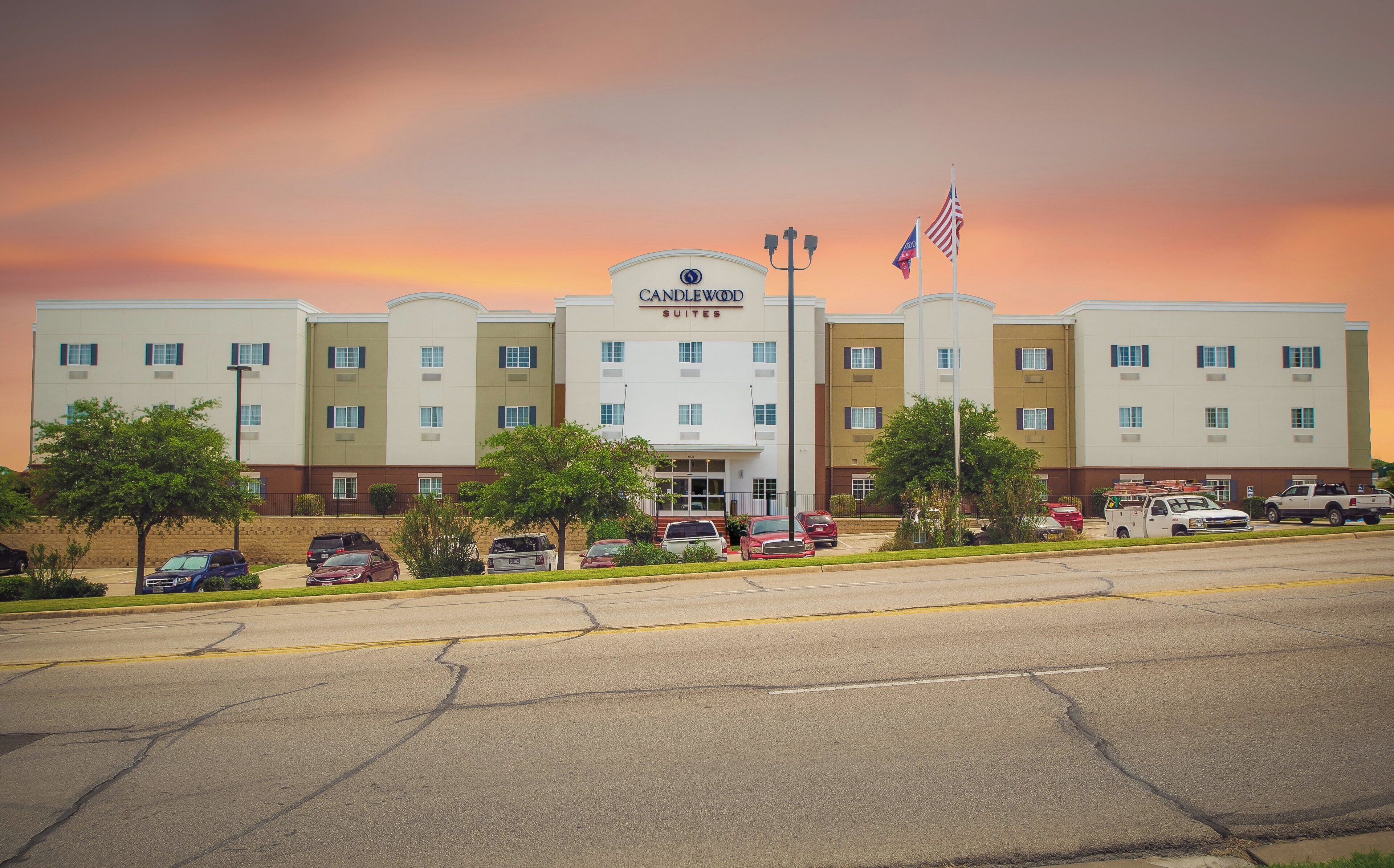A hotel with multiple floors, a central entrance, and a parking lot with several cars.